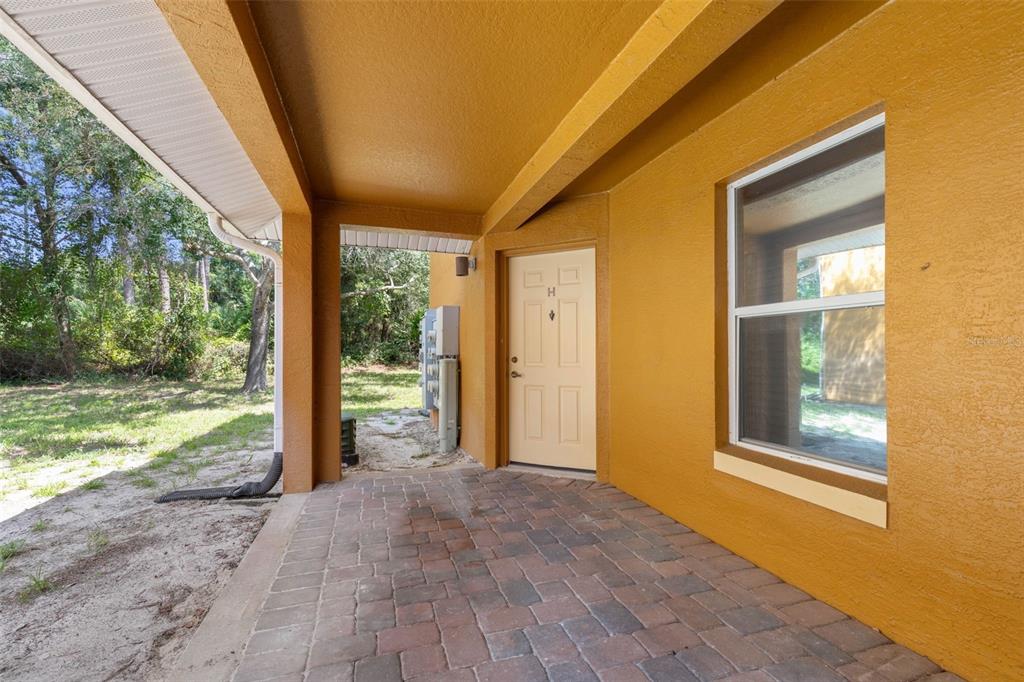 A covered patio with brick pavers leads to a beige door on a yellow exterior wall — 4600 E MOODY BOULEVARD UNIT 7H, BUNNELL, FL