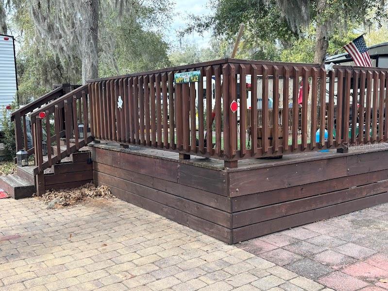A wooden deck with railings and stairs sits on a paved patio area — 25146 NE 140TH LOOP UNIT 71, SALT SPRINGS, FL