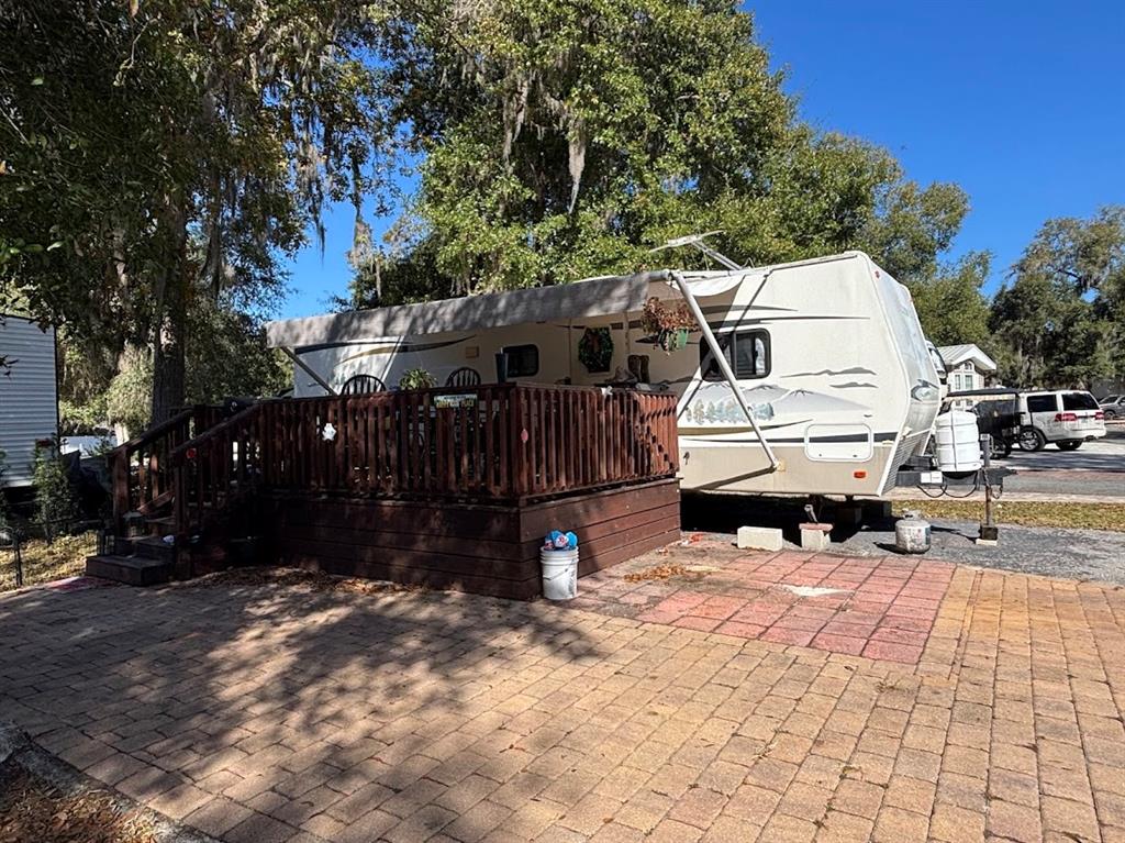 A travel trailer with an attached wooden deck sits on a paved patio under trees — 25146 NE 140TH LOOP UNIT 71, SALT SPRINGS, FL