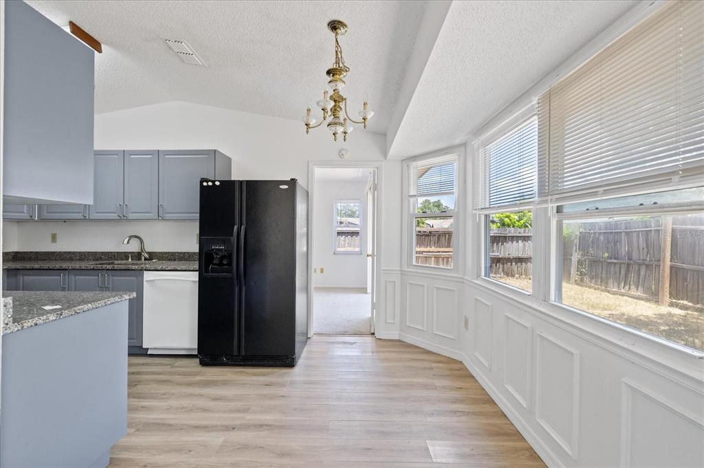 A kitchen with blue cabinets, a black refrigerator, and a dining area with large windows — 5102 MEADOWLARK LANE, NEW PORT RICHEY, FL