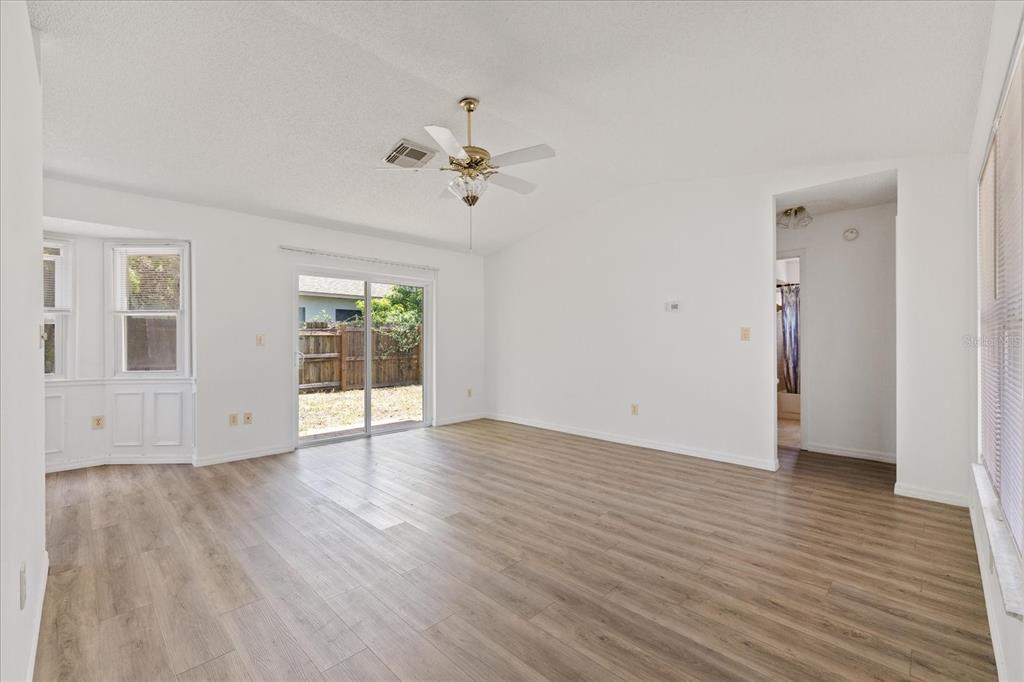 An empty living room features light wood-look flooring, a ceiling fan, and a sliding glass door — 5102 MEADOWLARK LANE, NEW PORT RICHEY, FL