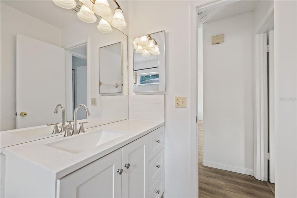 A white bathroom vanity with a sink, mirror, and light fixture sits beside a doorway — 5102 MEADOWLARK LANE, NEW PORT RICHEY, FL