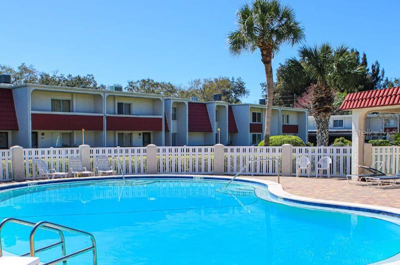 A swimming pool sits in front of a multi-story apartment building with a white fence — 2900 LICHEN LANE UNIT B, CLEARWATER, FL