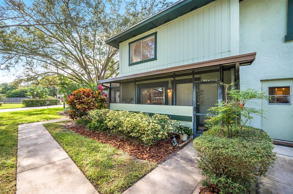 A two-story building exterior features a screened-in porch, light green siding, and landscaped front yard — 2900 LICHEN LANE UNIT B, CLEARWATER, FL