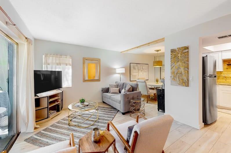 A living room features a gray sofa, a television, and an adjacent dining area — 2900 LICHEN LANE UNIT B, CLEARWATER, FL