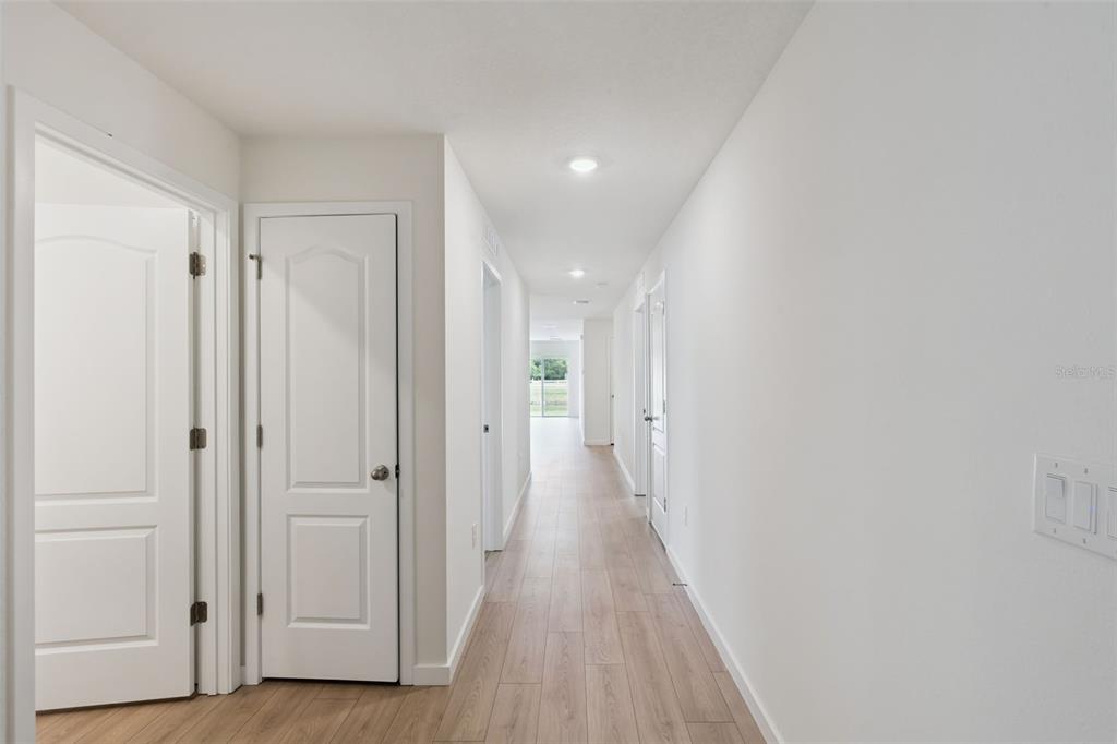 A long hallway with light wood-look flooring leads to a bright room with a sliding door — 1026 COMMONS WAY, PORT ORANGE, FL