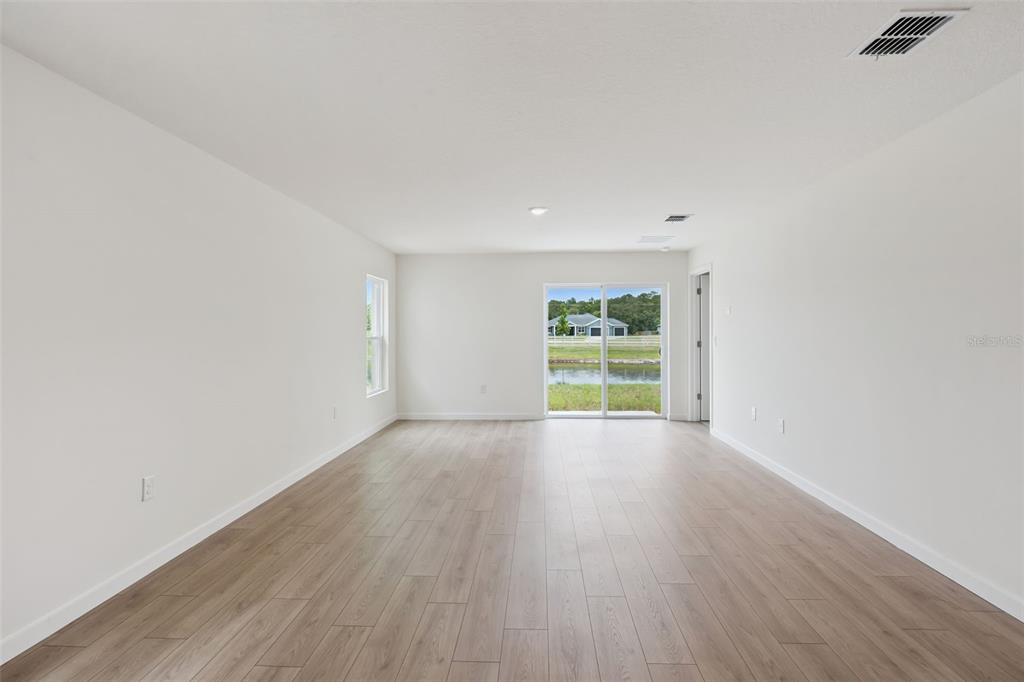 An empty room with light wood-look flooring, white walls, and a sliding glass door — 1026 COMMONS WAY, PORT ORANGE, FL