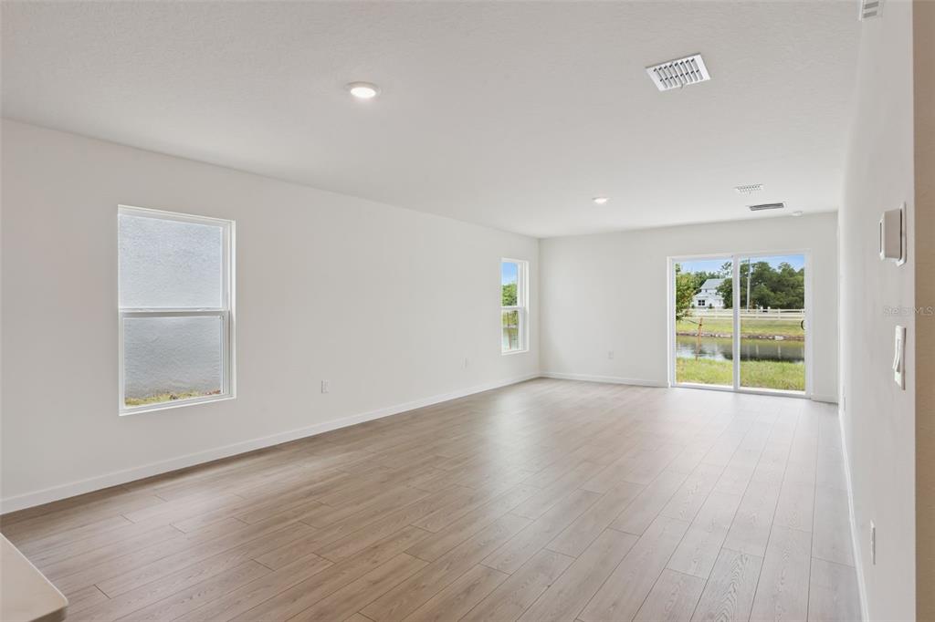 An empty room with white walls, light wood-look flooring, recessed lighting, and sliding glass doors — 1026 COMMONS WAY, PORT ORANGE, FL