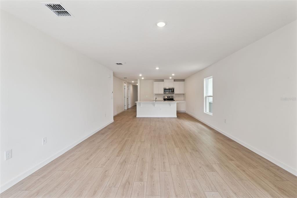 A long, open-concept living area features light wood-look flooring and a kitchen with white cabinets — 1026 COMMONS WAY, PORT ORANGE, FL