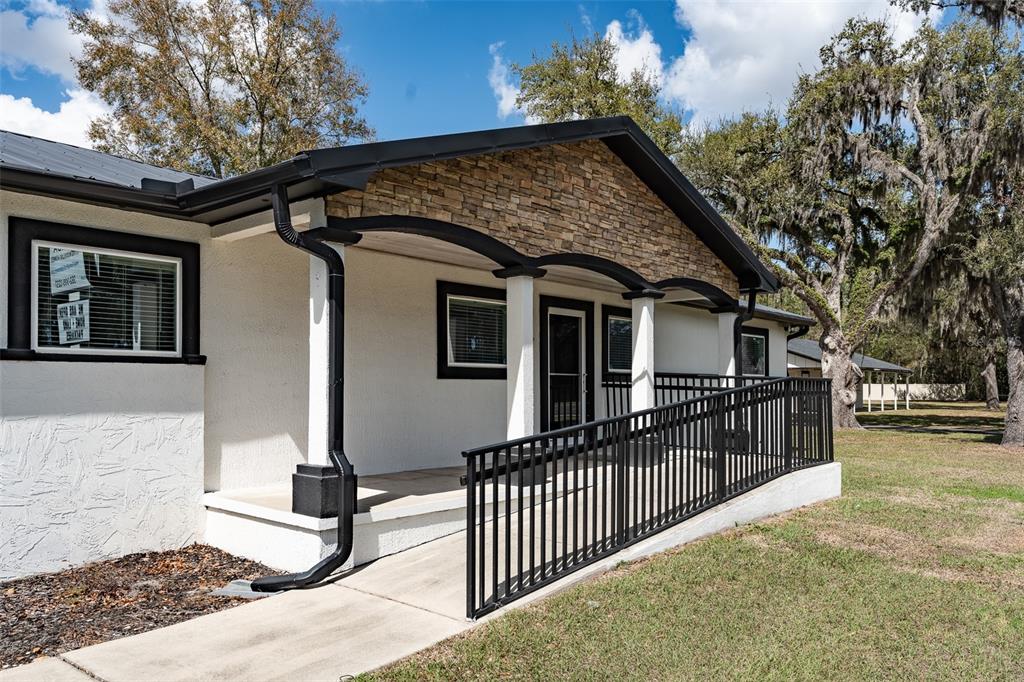 A white house exterior features a stone-accented porch with a black metal wheelchair ramp — 7265 SW HIGHWAY 200, OCALA, FL