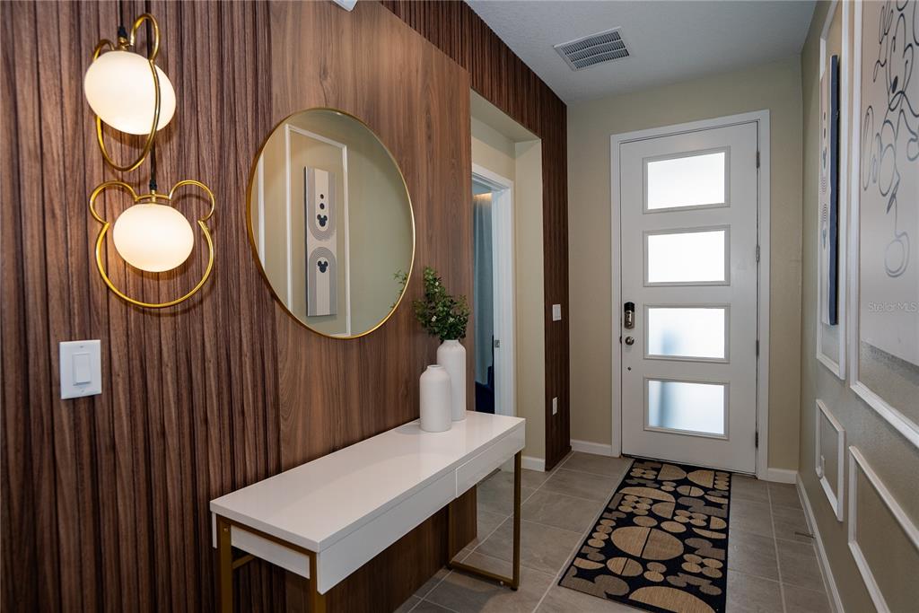 An entryway features a wood-paneled wall, a white console table, a round mirror, and lighting — 2379 DISTANT SUN TRAIL, KISSIMMEE, FL