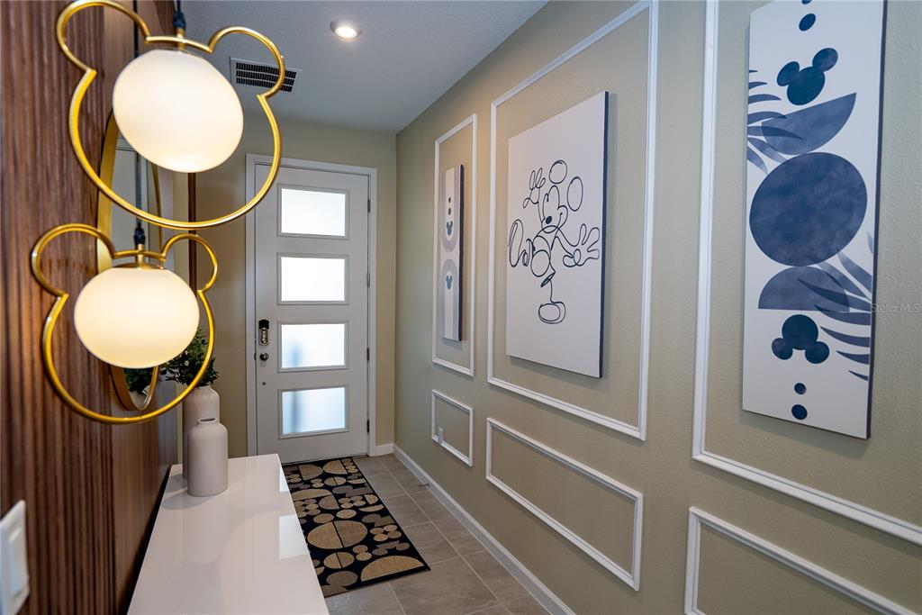 An entryway features Mickey Mouse-themed wall art, light fixtures, and a white door with glass panels — 2379 DISTANT SUN TRAIL, KISSIMMEE, FL