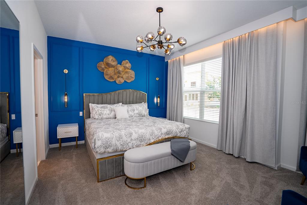 A bedroom features a blue accent wall, a grey upholstered bed, and a modern chandelier — 2379 DISTANT SUN TRAIL, KISSIMMEE, FL
