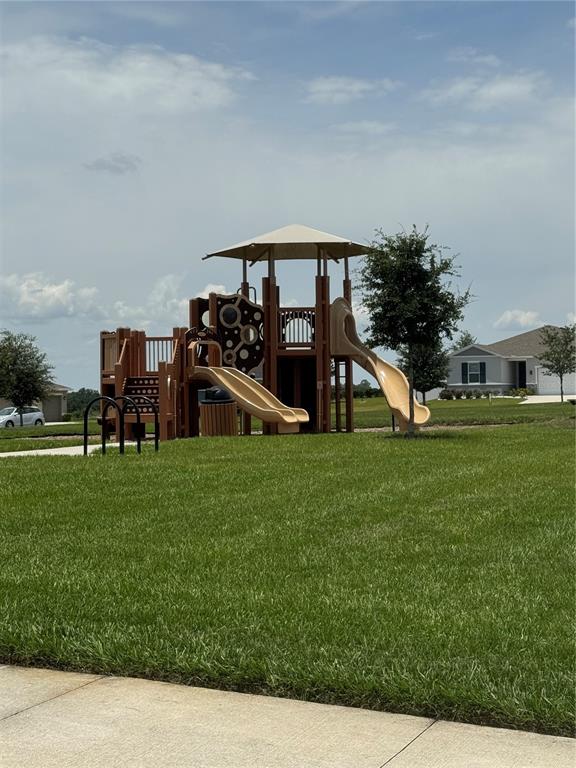 A playground structure with two slides sits on a grassy lawn near suburban houses — 1459 GERANIUM DRIVE, MASCOTTE, FL