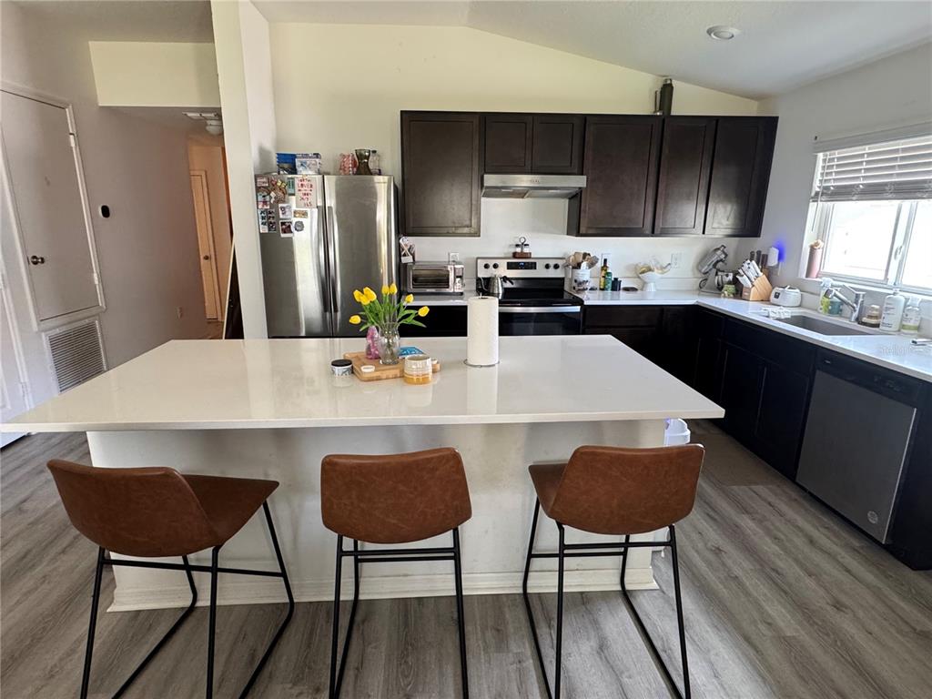 A kitchen features dark cabinets, white countertops, a central island with three stools, and stainless appliances — 1459 GERANIUM DRIVE, MASCOTTE, FL