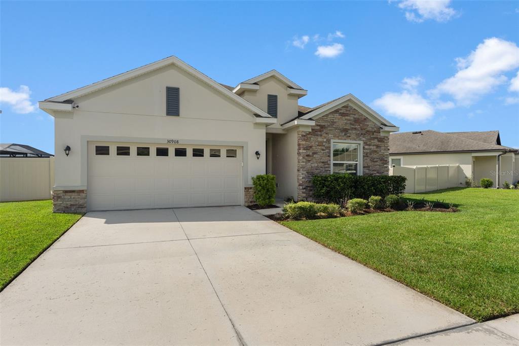 A single-story house with a beige stucco exterior, stone accents, and a two-car garage — 30908 PARROT REEF COURT, WESLEY CHAPEL, FL