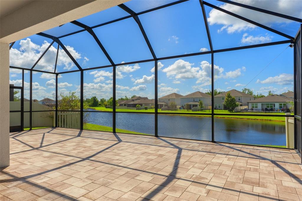 A screened-in patio with paver flooring overlooks a pond and neighboring houses — 30908 PARROT REEF COURT, WESLEY CHAPEL, FL