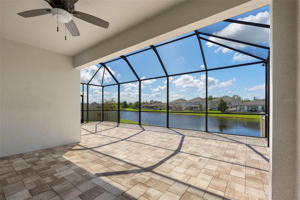 A covered patio with paver flooring and a screened enclosure overlooking a lake — 30908 PARROT REEF COURT, WESLEY CHAPEL, FL