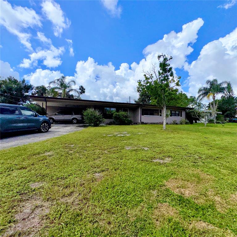 A single-story house with a carport and a large front lawn under a cloudy sky — 105 DRUID HILLS ROAD, TEMPLE TERRACE, FL