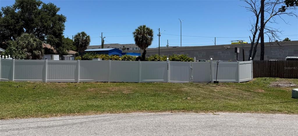 A white vinyl privacy fence encloses a grassy yard with a gate and nearby trees — 1455 LACONIA DRIVE E, CLEARWATER, FL