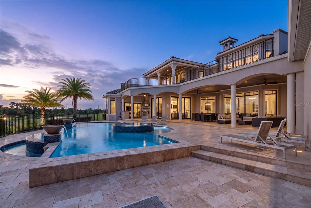A luxury home exterior features a multi-level patio, a swimming pool, and a second-story balcony — 7829 PALMILLA COURT, KISSIMMEE, FL