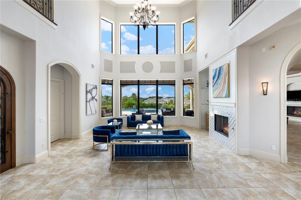 A bright, two-story living room features blue velvet furniture, a fireplace, and large windows — 7829 PALMILLA COURT, KISSIMMEE, FL