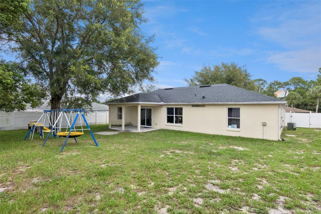 The backyard of a single-story house features a swing set and a covered patio — 939 CLOVERLEAF BOULEVARD, DELTONA, FL