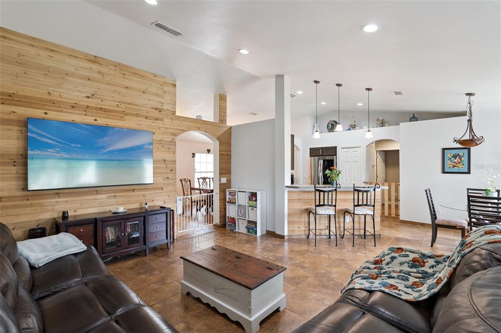 A living room features a wood-paneled accent wall, tile flooring, and an open kitchen area — 939 CLOVERLEAF BOULEVARD, DELTONA, FL