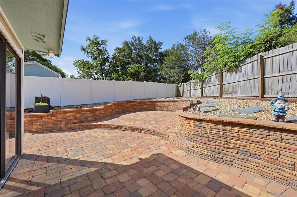 A backyard patio features tiered stone retaining walls, paver flooring, and a wooden privacy fence — 17 HIBISCUS COURT, EUSTIS, FL