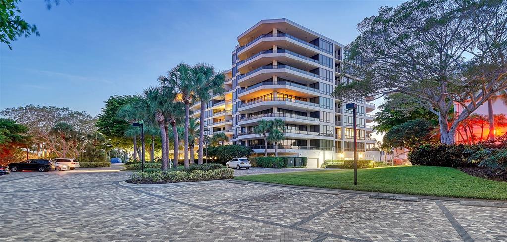 A multi-story residential building stands behind a paved parking lot with palm trees and landscaping — 535 SANCTUARY DRIVE UNIT C807, LONGBOAT KEY, FL
