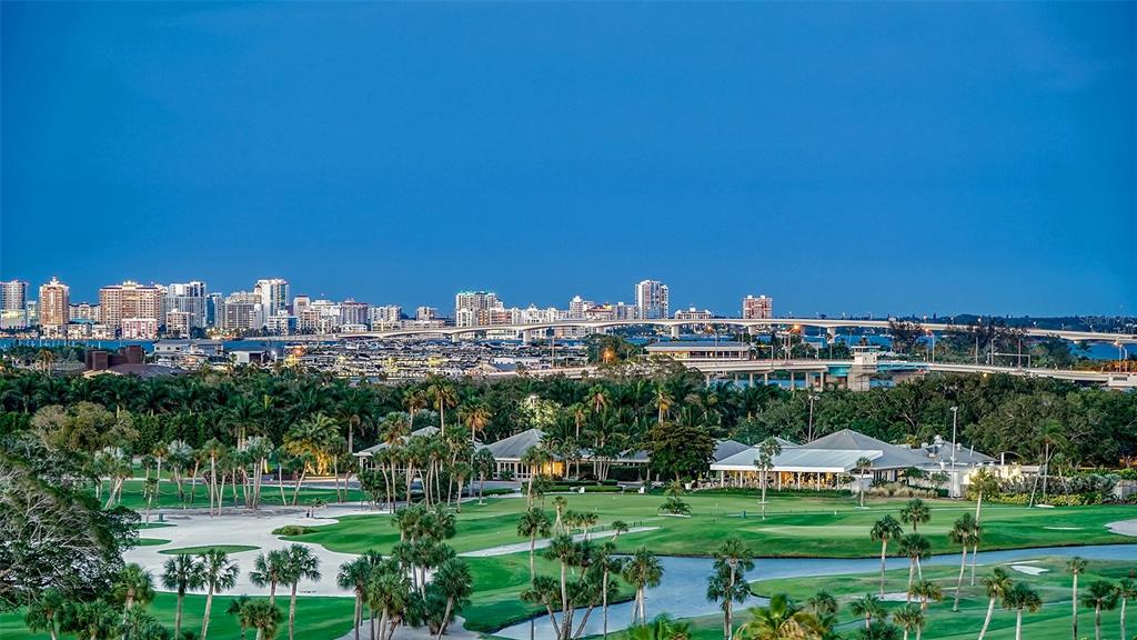 An elevated view of a golf course with a city skyline and bridge in the background — 535 SANCTUARY DRIVE UNIT C807, LONGBOAT KEY, FL