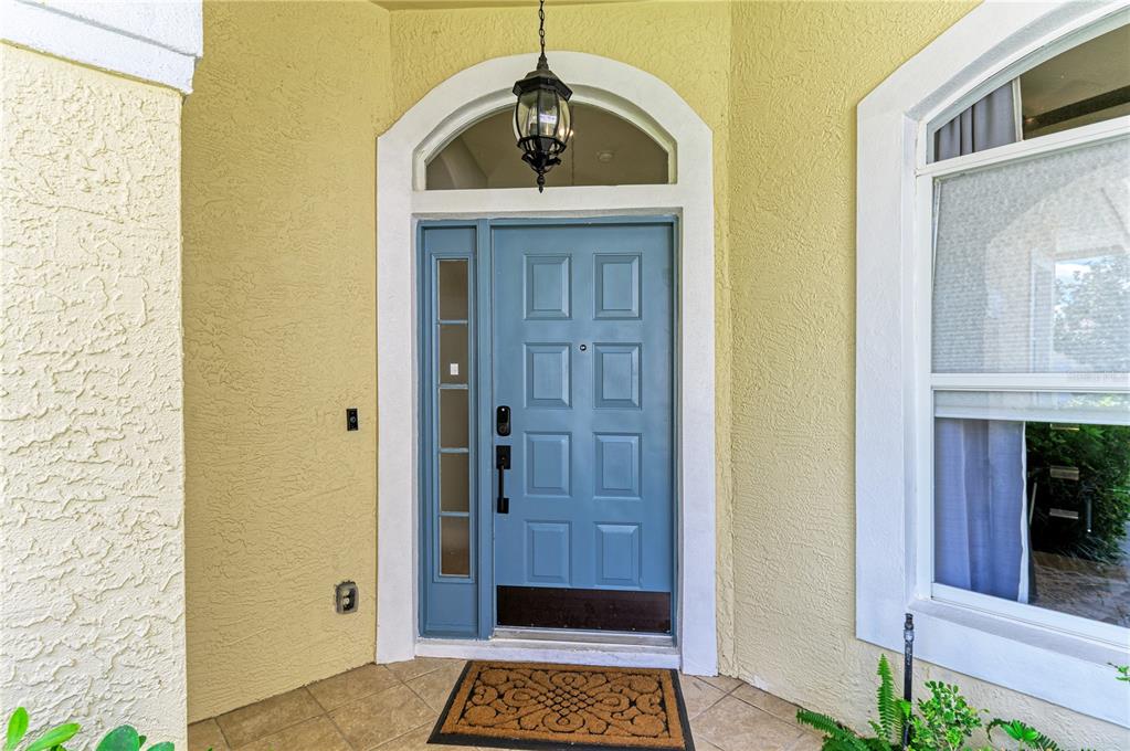 A blue front door with a side window and arched transom sits under a porch — 6622 OAKBROOKE CIRCLE, BRADENTON, FL