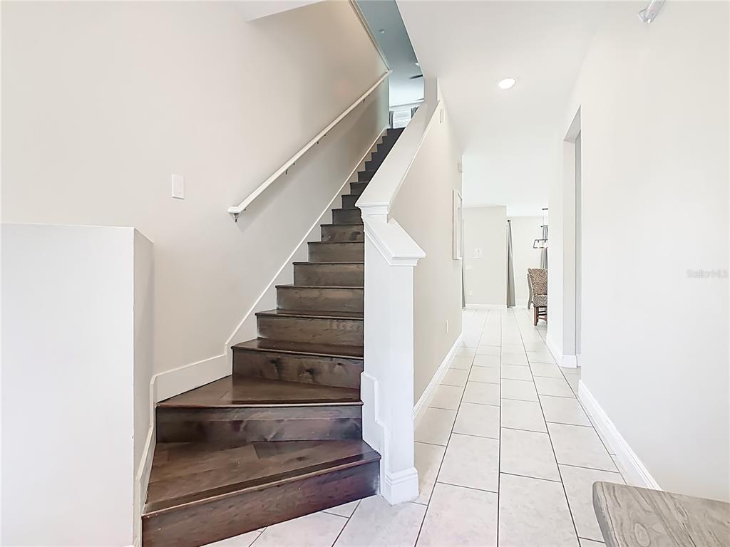 A staircase with dark wood treads and white risers sits beside a tiled hallway — 267 SOUTHFIELD STREET, KISSIMMEE, FL