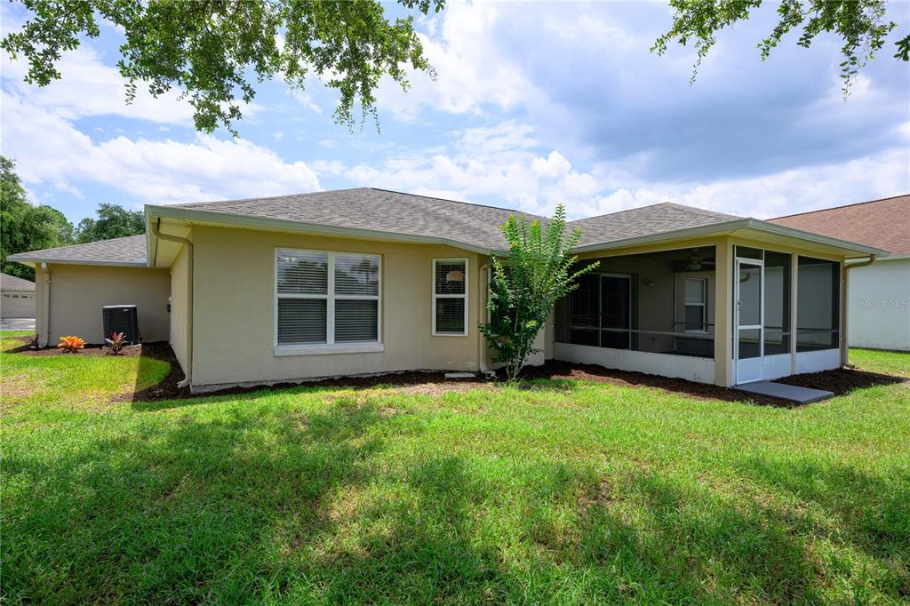 The exterior of a tan house features a screened-in porch and a grassy backyard — 1712 ARASH CIRCLE, PORT ORANGE, FL