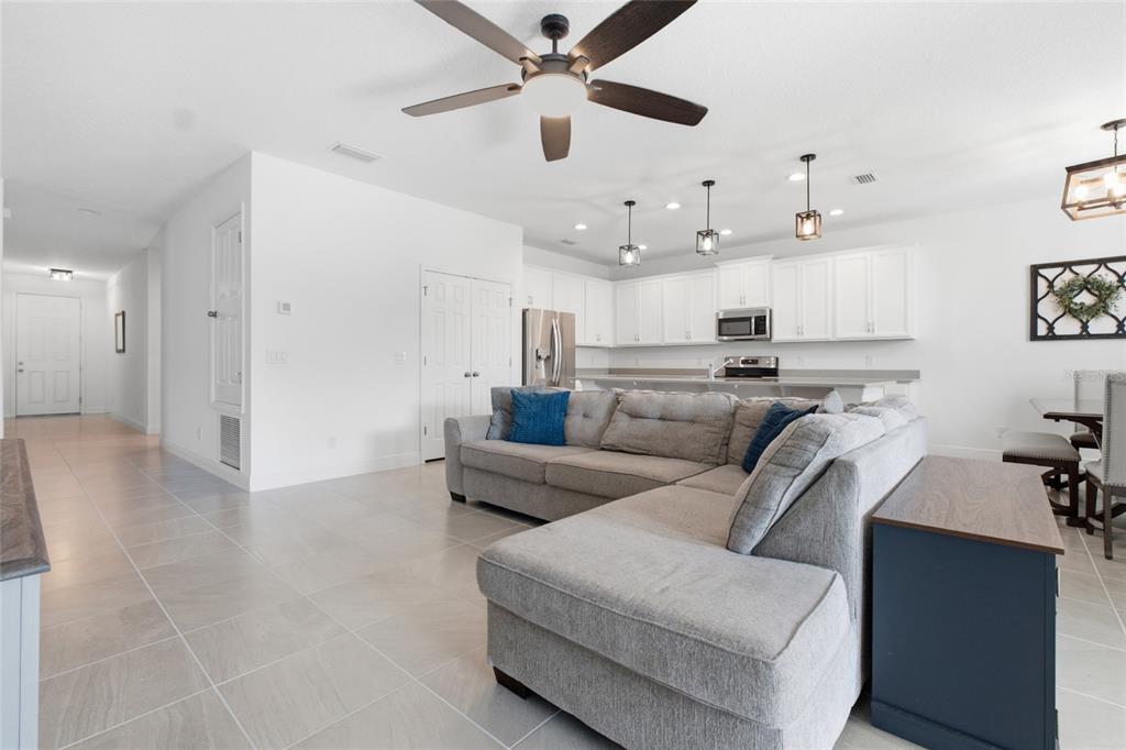 A living room with light tile floors and a gray sectional sofa faces an open kitchen — 180 JENSEN DRIVE, GROVELAND, FL