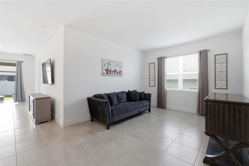 A living room features a dark gray sofa, light tile flooring, and a large window — 180 JENSEN DRIVE, GROVELAND, FL