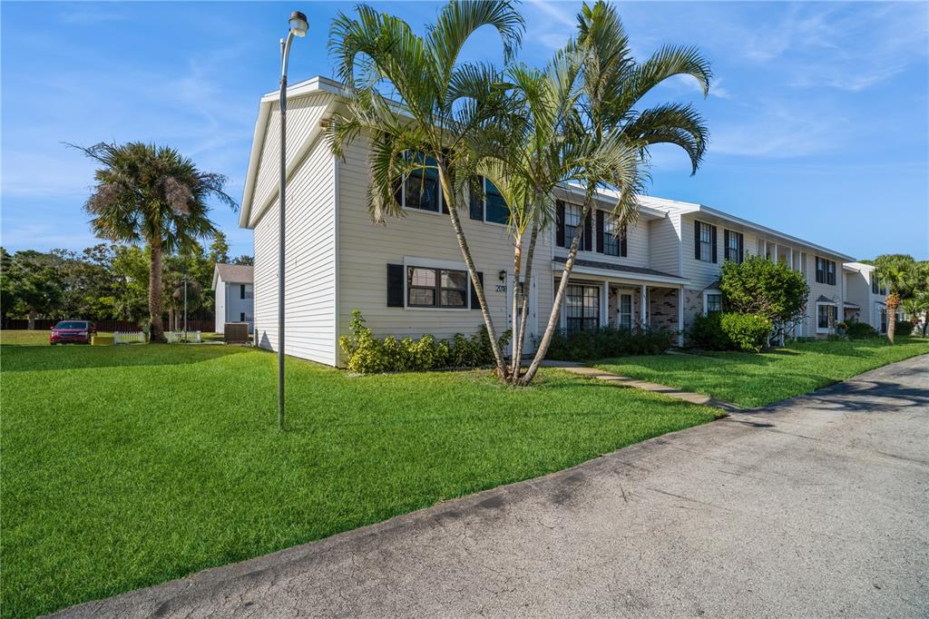 A two-story townhouse with light siding, palm trees, and a grassy front yard — 2018 MANOR DRIVE NE, PALM BAY, FL