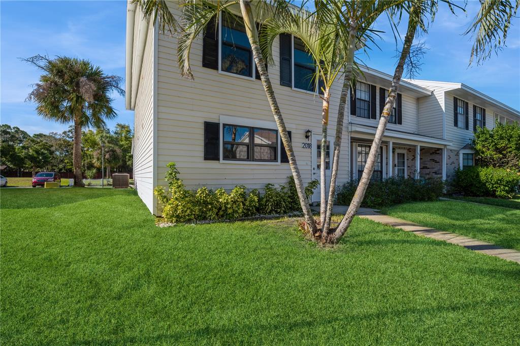 A two-story townhouse with light siding, black shutters, and palm trees in the front yard — 2018 MANOR DRIVE NE, PALM BAY, FL