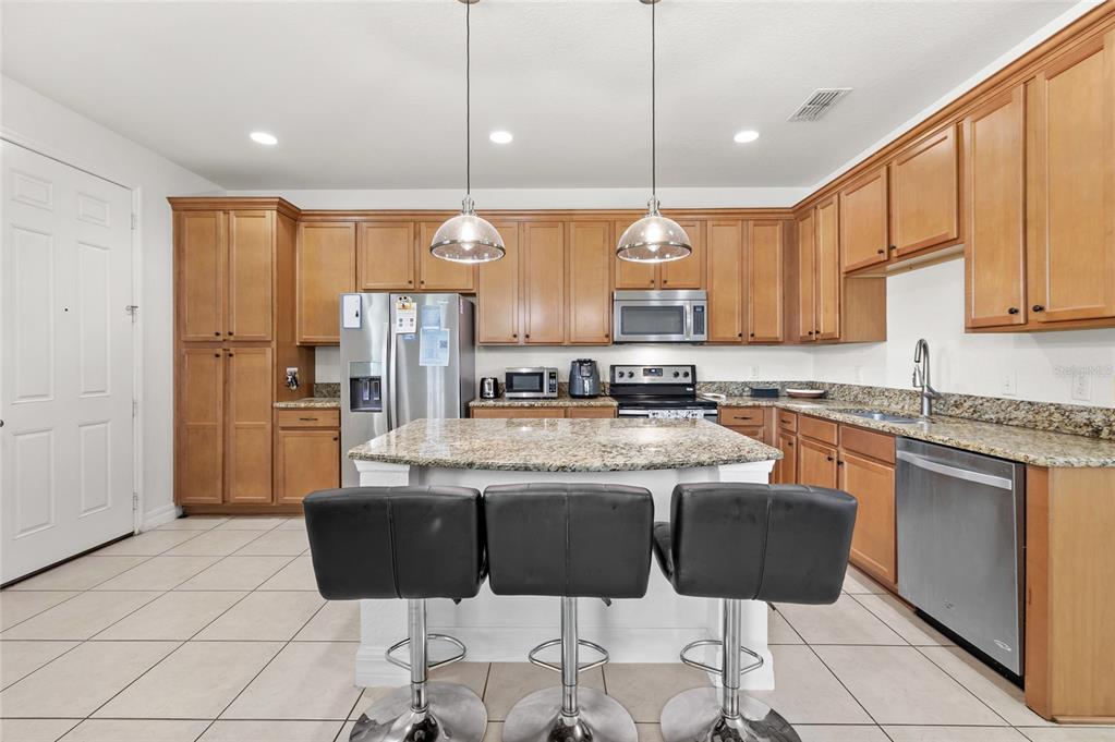 A kitchen with wood cabinets, granite countertops, stainless steel appliances, and a central island — 10155 EAGLE CREEK CENTER BOULEVARD, ORLANDO, FL
