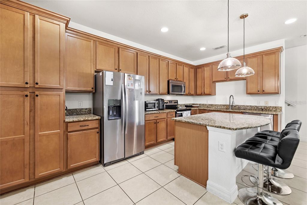 A kitchen with wood cabinets, granite countertops, stainless steel appliances, and a breakfast bar island — 10155 EAGLE CREEK CENTER BOULEVARD, ORLANDO, FL