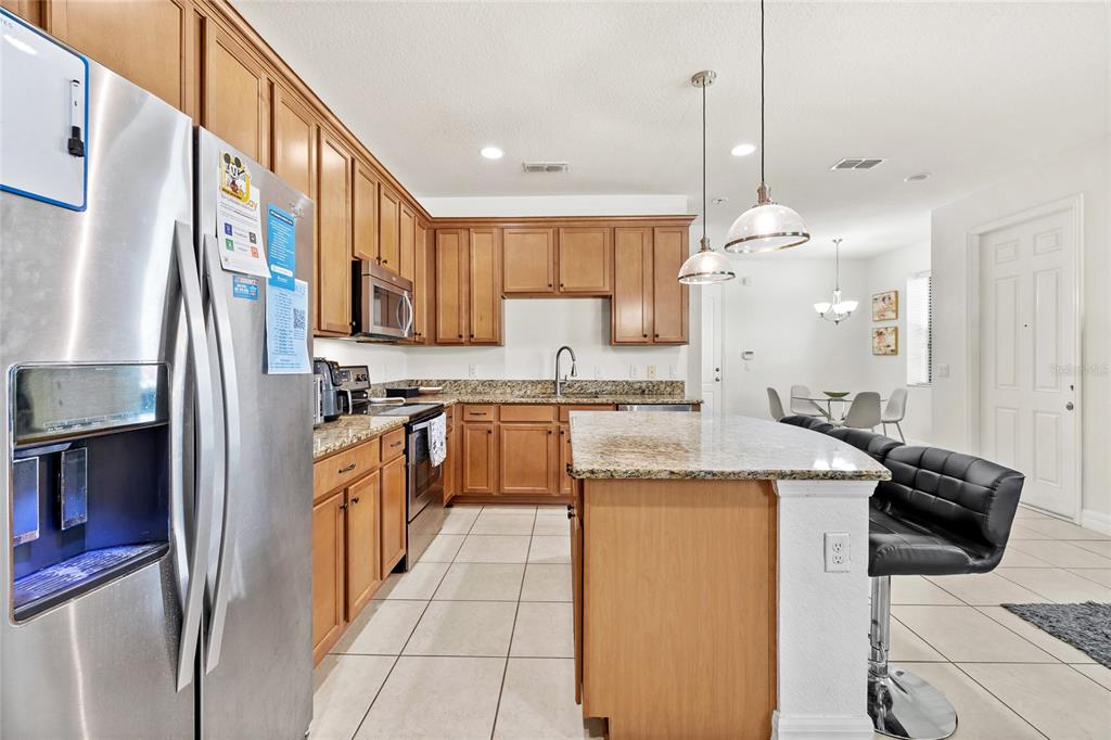 A kitchen features wood cabinets, granite countertops, a stainless steel refrigerator, and a breakfast island — 10155 EAGLE CREEK CENTER BOULEVARD, ORLANDO, FL