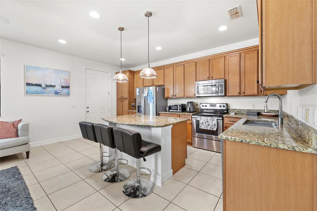A kitchen features wood cabinets, granite countertops, stainless steel appliances, and a breakfast bar with stools — 10155 EAGLE CREEK CENTER BOULEVARD, ORLANDO, FL