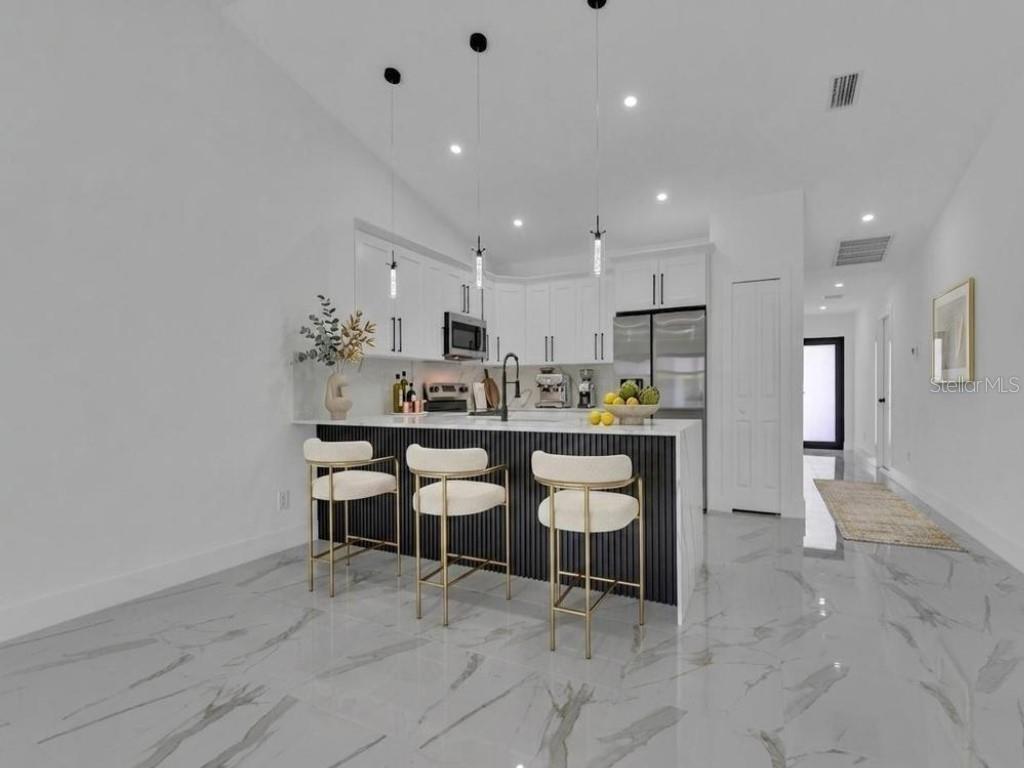 A modern kitchen features white cabinets, a black slatted island, and marble-look tile flooring — 4747 13TH STREET SW, LEHIGH ACRES, FL