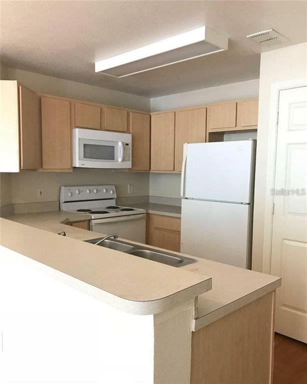 A kitchen features light wood cabinets, white appliances, and a breakfast bar with a sink — 2000 ERVING CIRCLE UNIT 102, OCOEE, FL