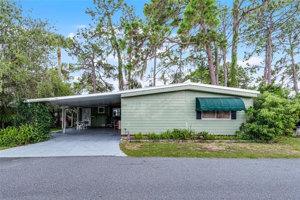 A single-story light green mobile home with a carport and a green window awning — 192 PALM MEADOWS DRIVE, EUSTIS, FL