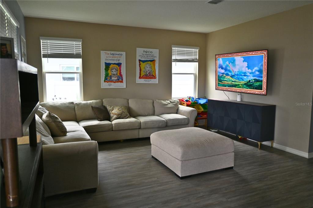 A living room features a beige sectional sofa, a matching ottoman, and a wall-mounted television — 2517 BISCOTTO CIRCLE, DAVENPORT, FL
