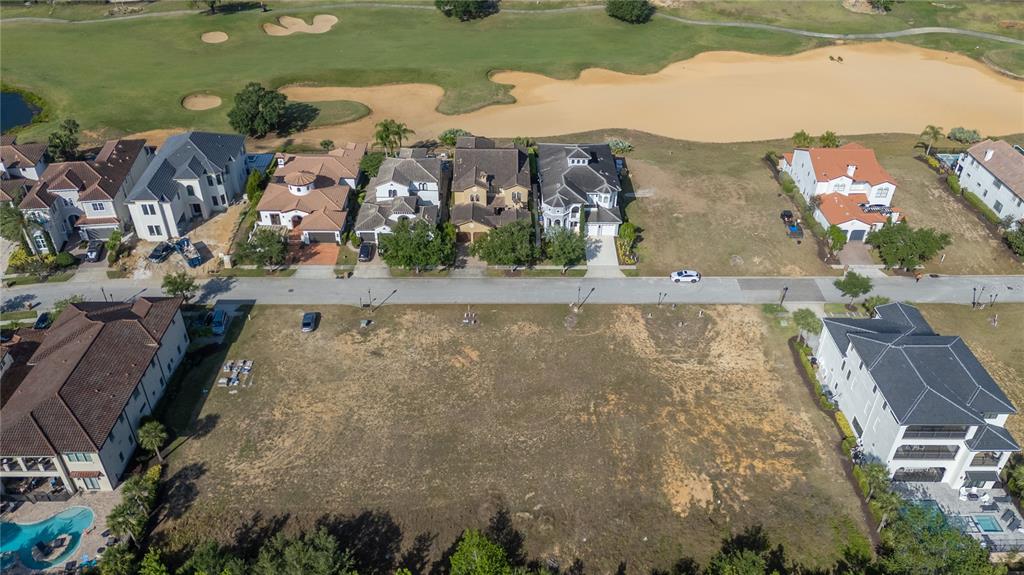 An aerial view shows a vacant residential lot situated between two large houses near a golf course — 570 MUIRFIELD LOOP, REUNION, FL