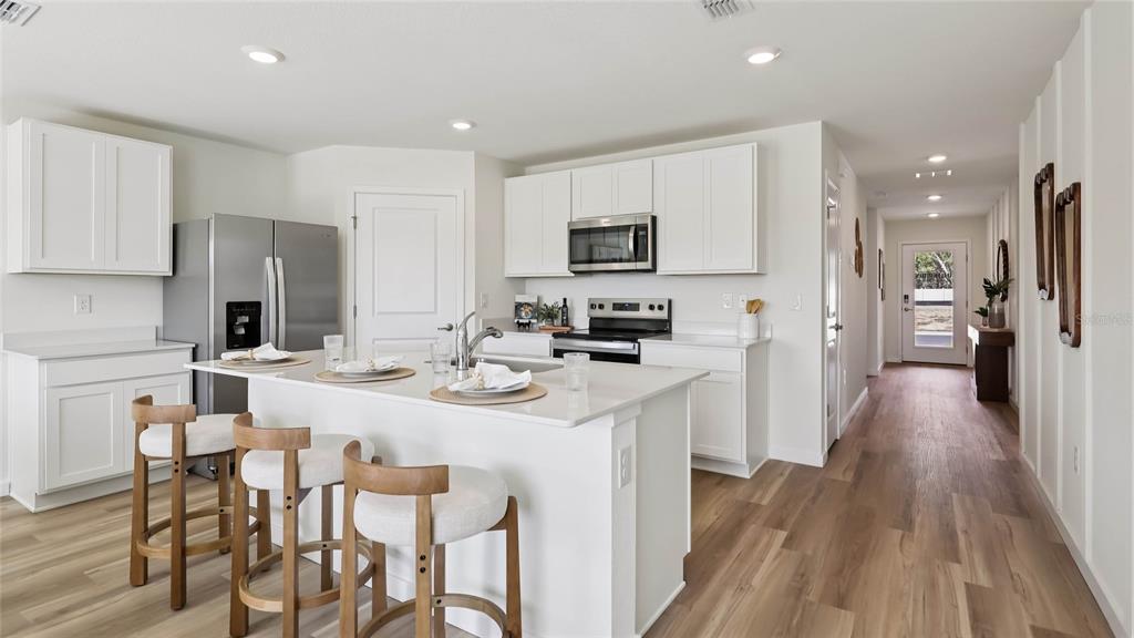 A modern kitchen features white cabinetry, a central island with bar stools, and wood flooring — 10174 SE 158TH LANE, SUMMERFIELD, FL