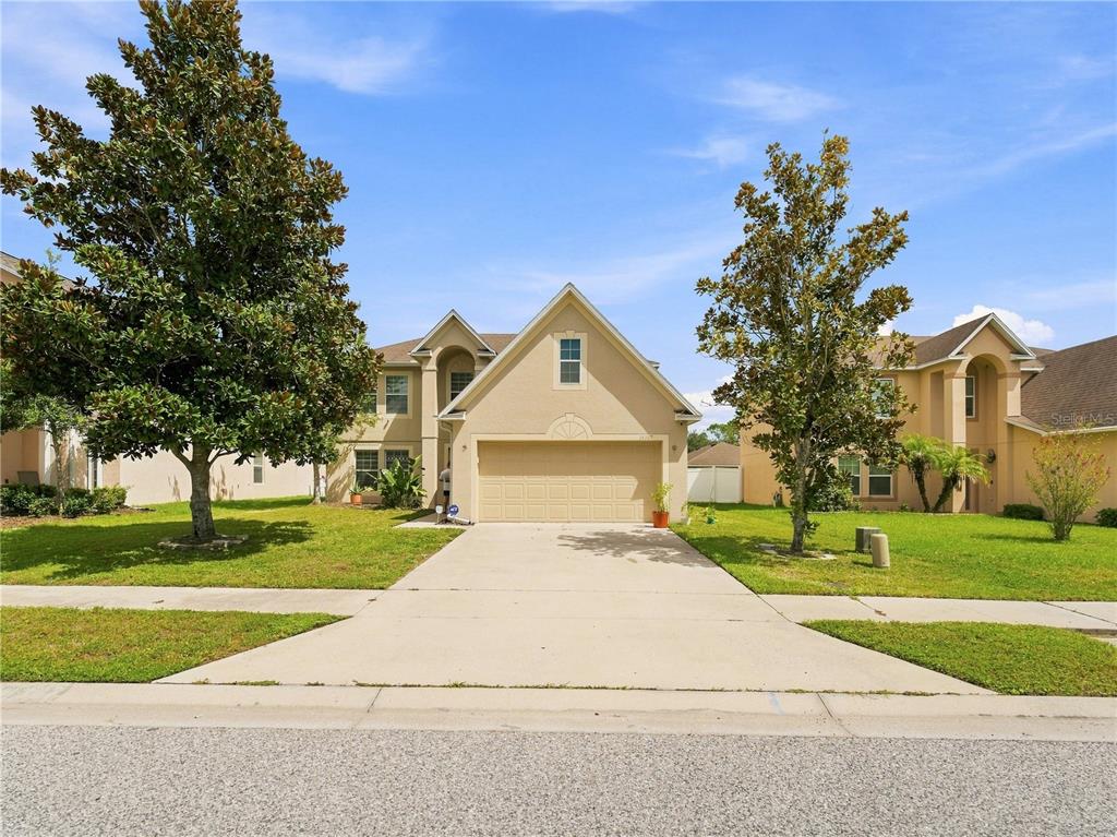 A two-story suburban house with a tan stucco exterior, a two-car garage, and two large trees — 14367 SALTBY PLACE, SPRING HILL, FL