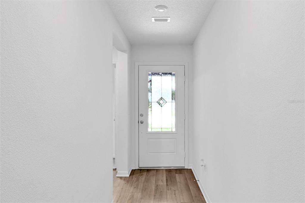 A white-walled entryway features wood-look flooring and a front door with a decorative glass insert — 153 PARKVIEW DRIVE, PALM COAST, FL